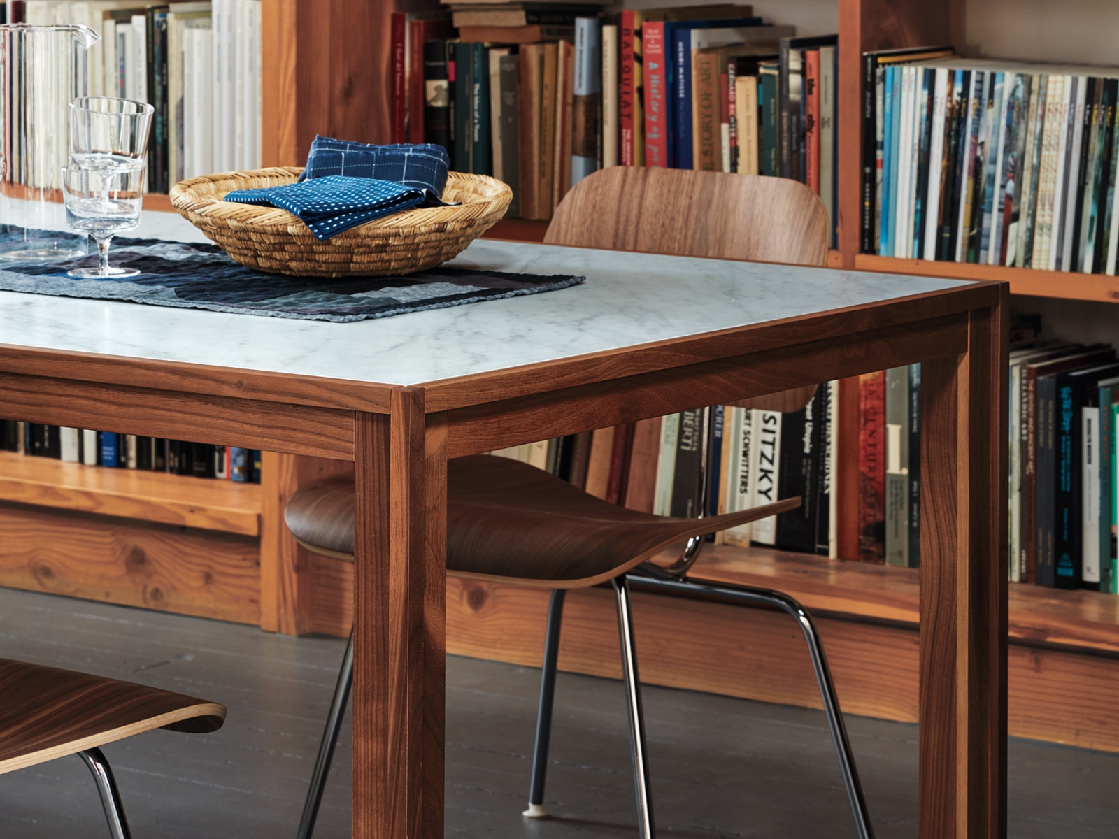 An Eames Moulded Plywood Dining Chair with a metal base sits at a rectangular table with bookshelves in the background.